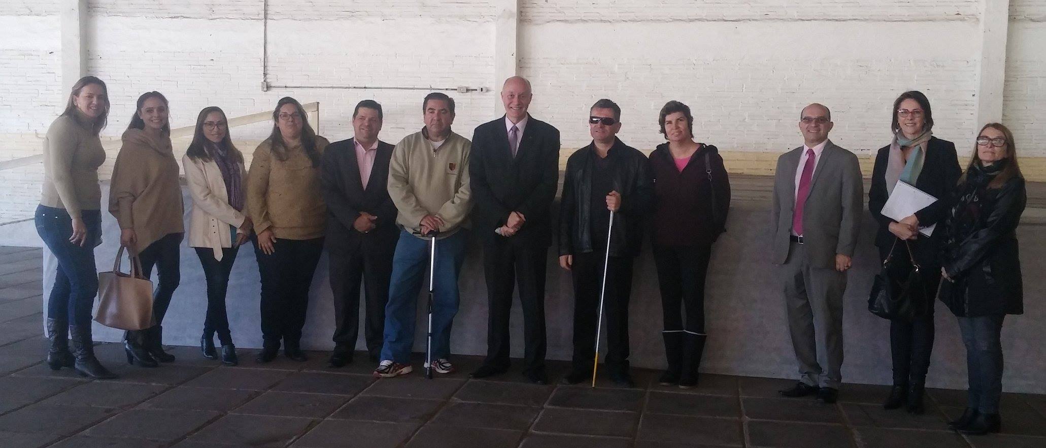 Integrantes da comissão organizadora da ExpoTAI, todos posicionados em frente ao palco. Ao fundo parede branca. Fim da descrição 